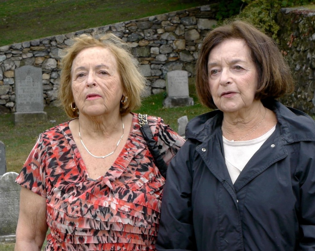 Sisters stand in a cemetery near their grandmother's grave.