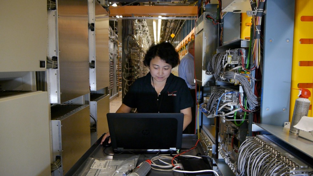 A woman works on a laptop in an industrial setting with wires.