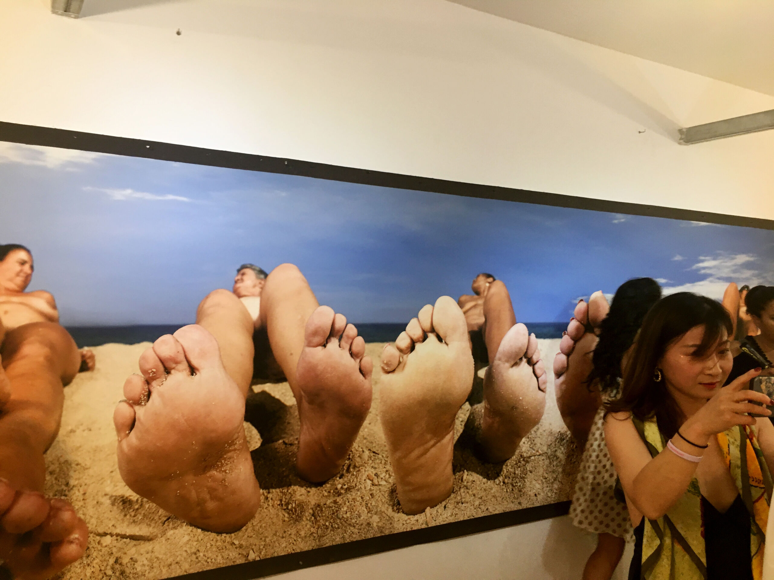 A woman stands before a very large photograph of human feet.