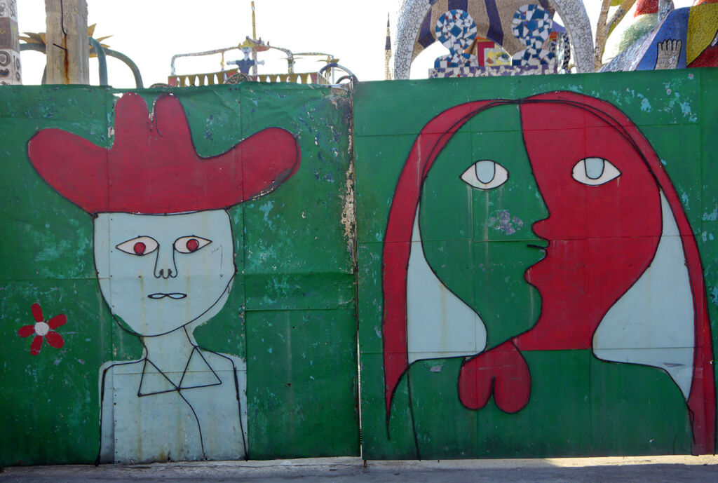 An old gate is painted with green and red images of a cowboy and woman in the style of Picasso.