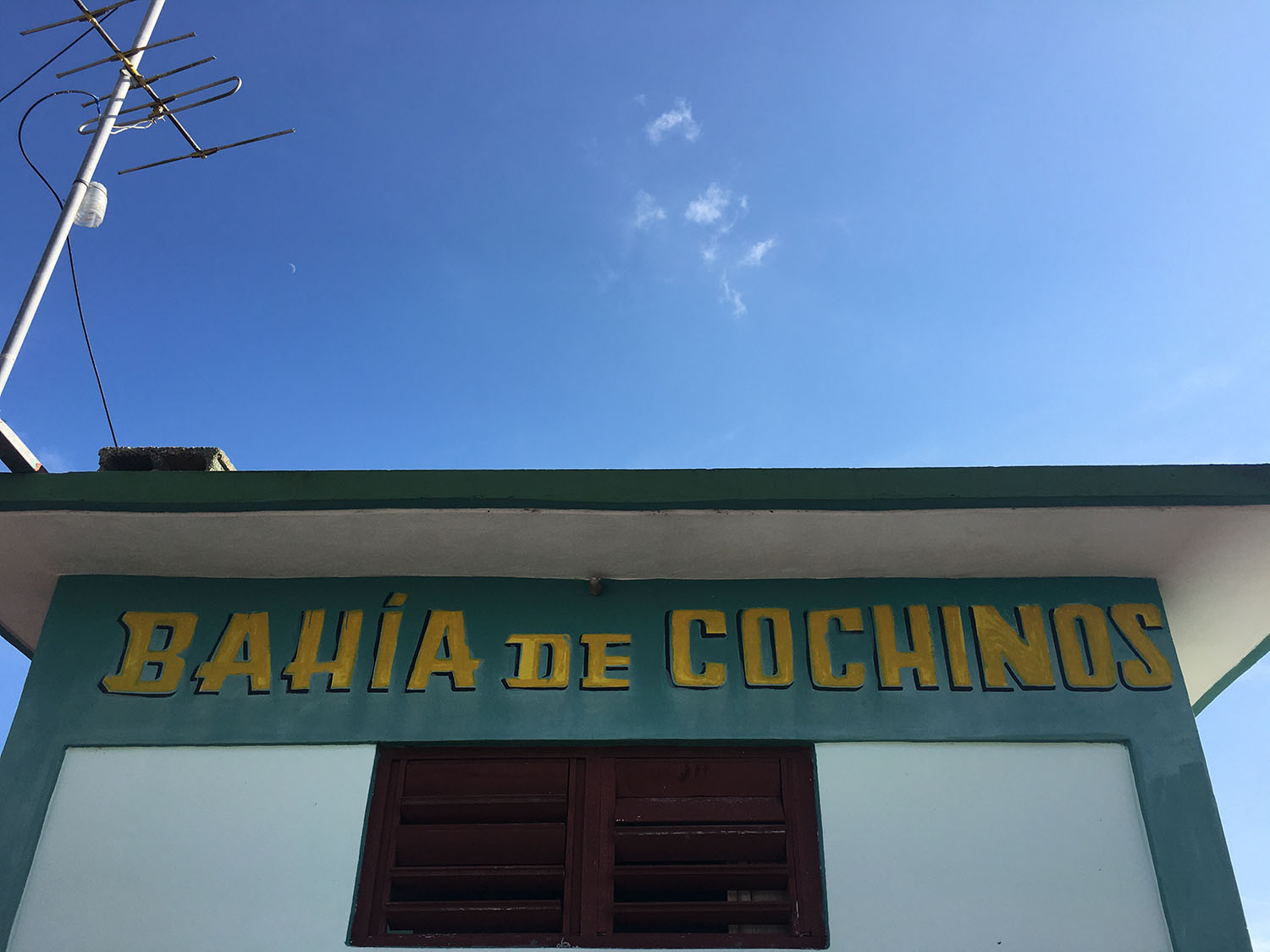 A painted aqua and yellow sign on a building reads "Bahia de Cochinos."