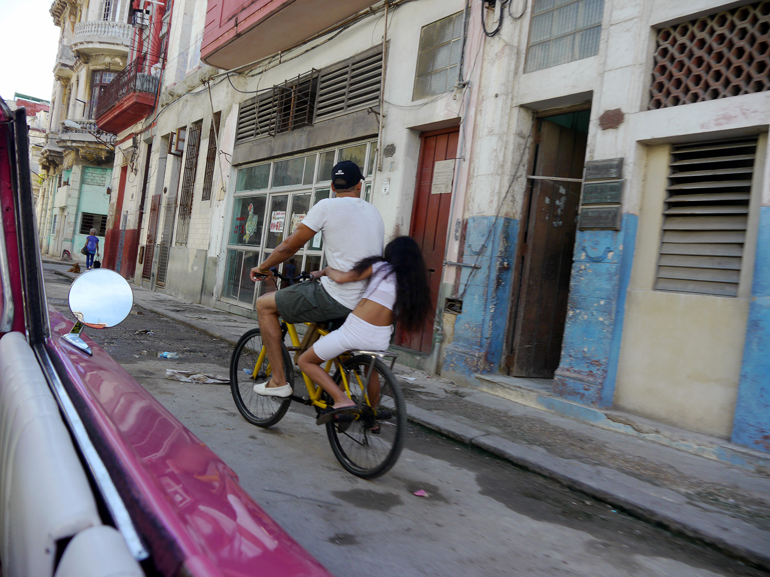 A girl holds on tight to a man on the back of a moving bicycle.