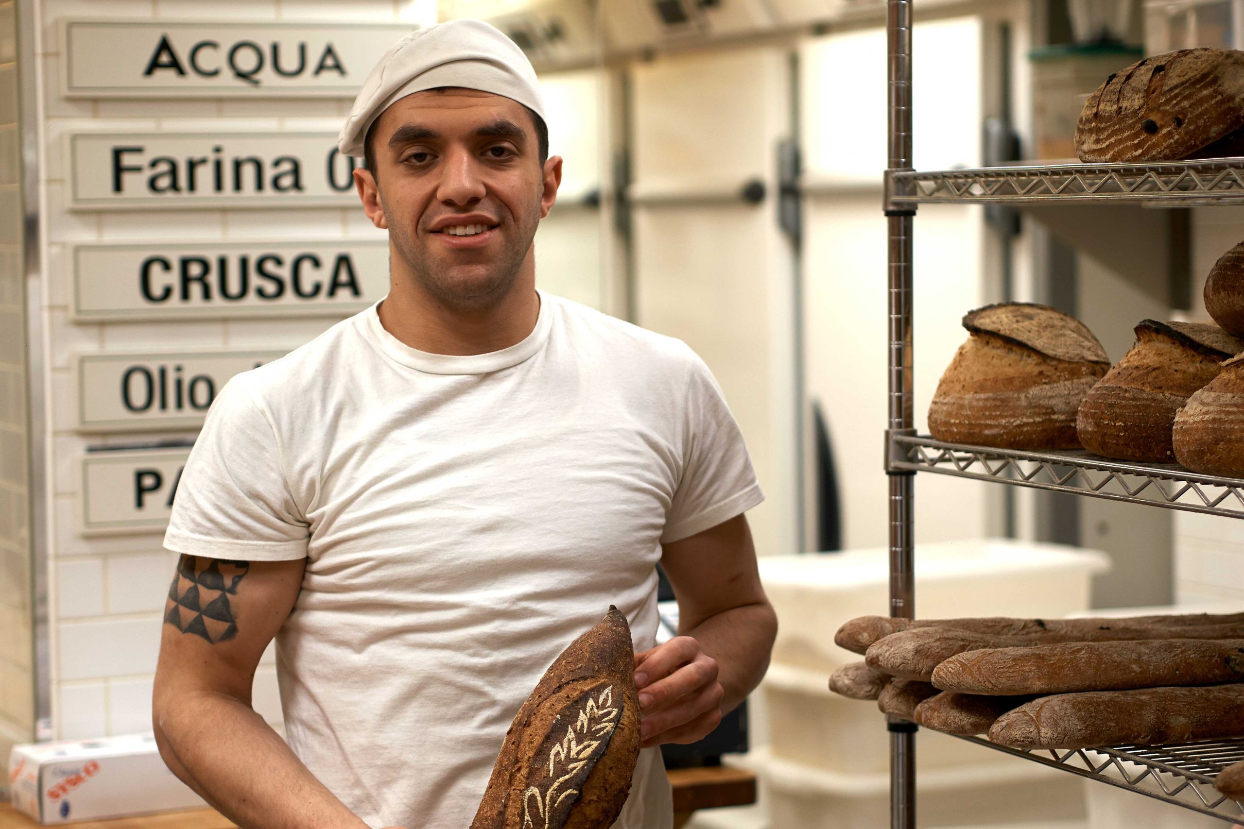 A baker poses with a loaf of artisan bread.