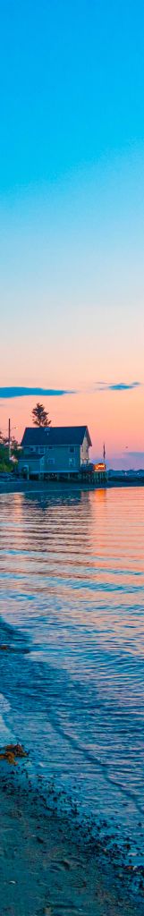 A narrow view of a house at sunset on a beach in Maine.