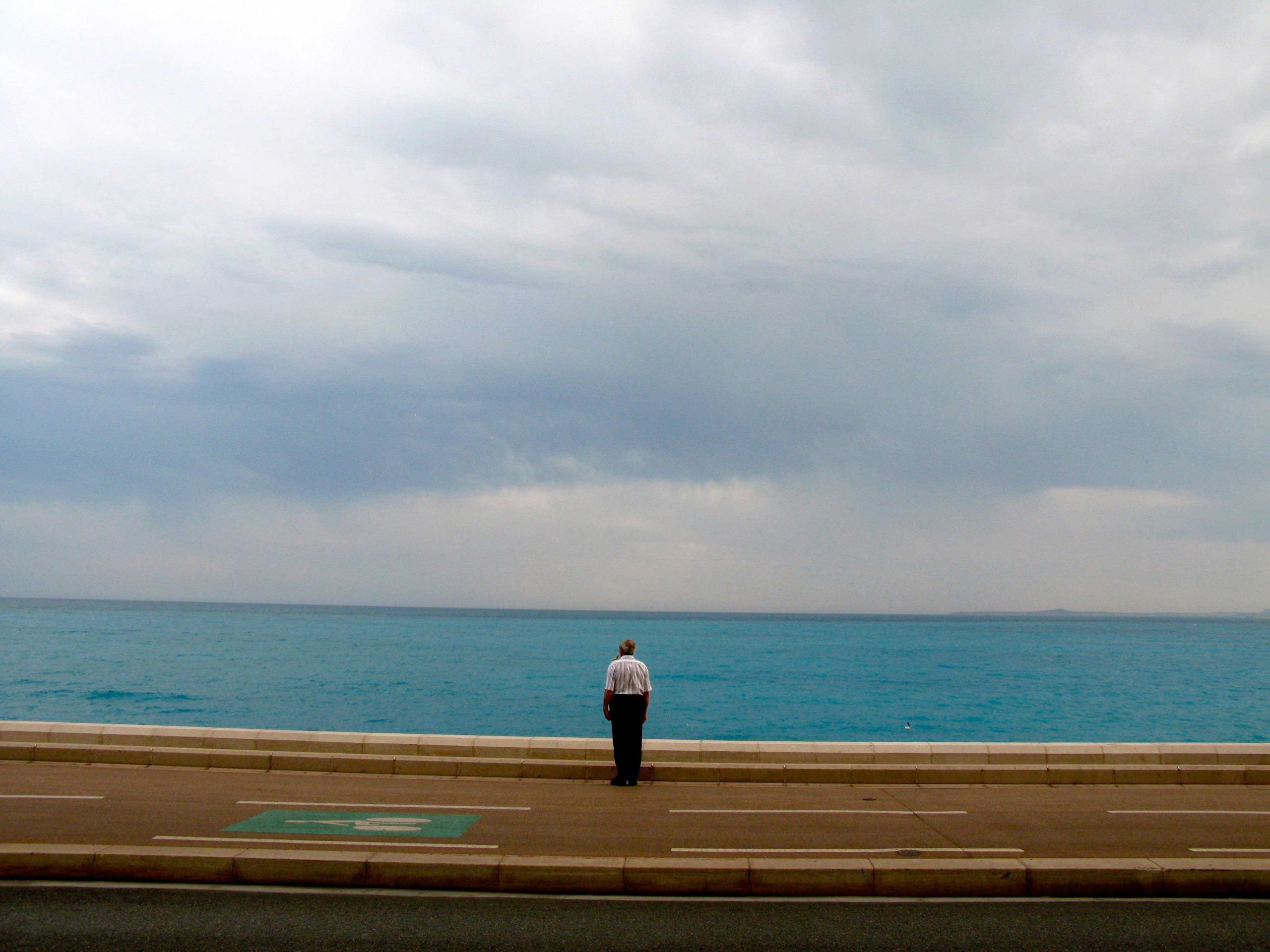 A man standing in the middle of a road before a bright blue ocean.
