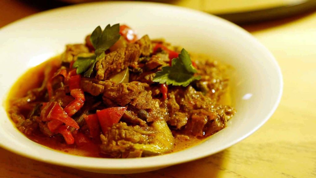 A bowl of steak with red and green peppers.