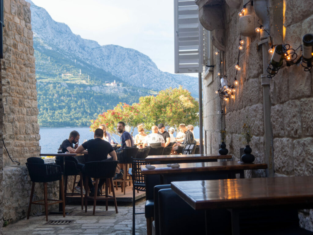 People dining outside at tables with grand mountains in the background.