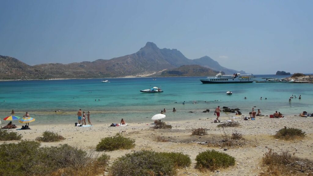 A sandy beach with turquoise water and a mountain in the background.